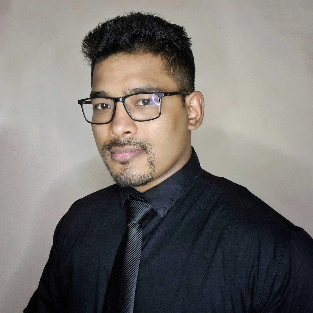 Prajal Bariya in a black shirt and striped black tie, wearing black rectangular glasses